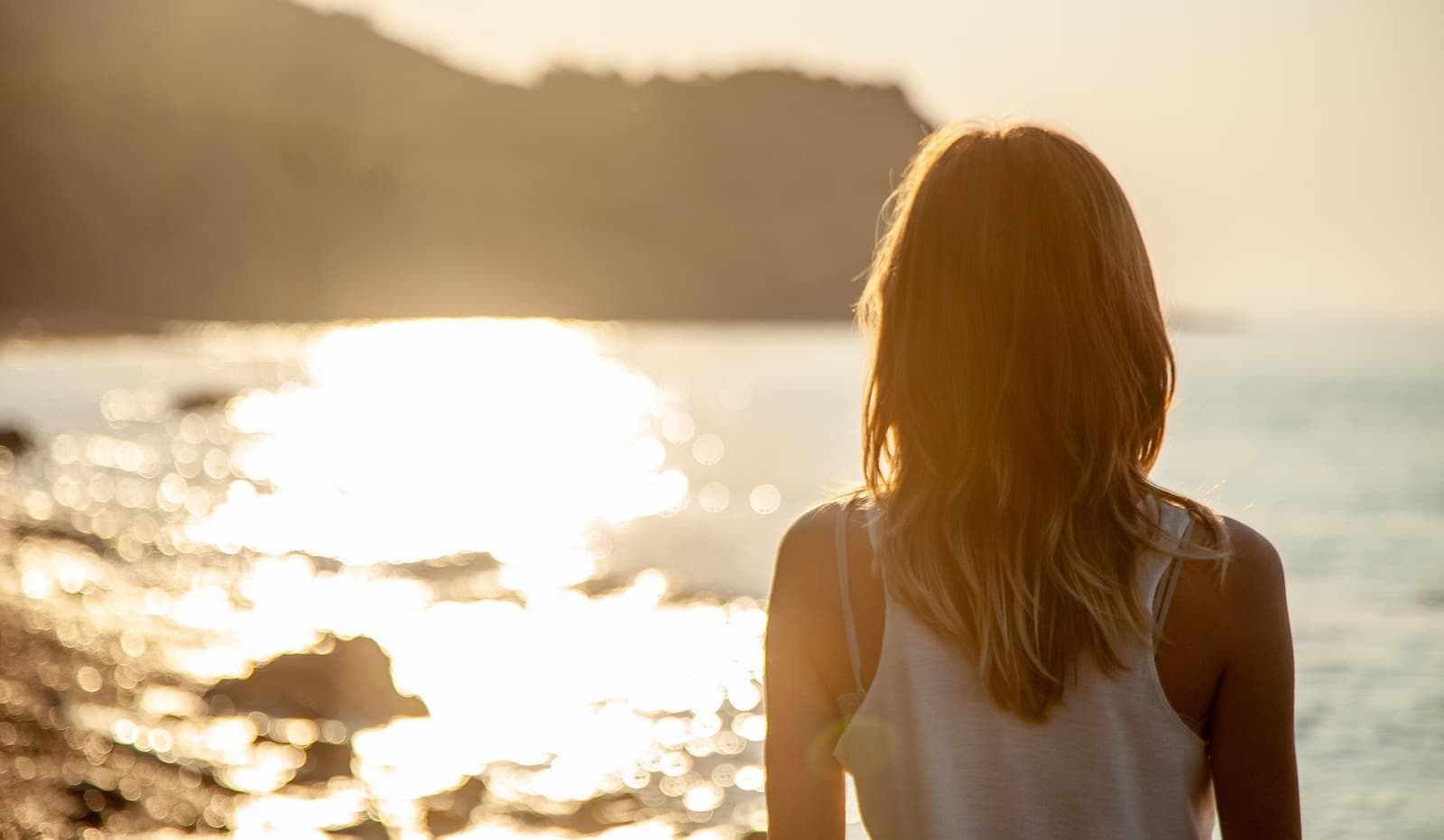 Someone seen from behind, looking out over a sea catching the light — the quiet before reading a relationship