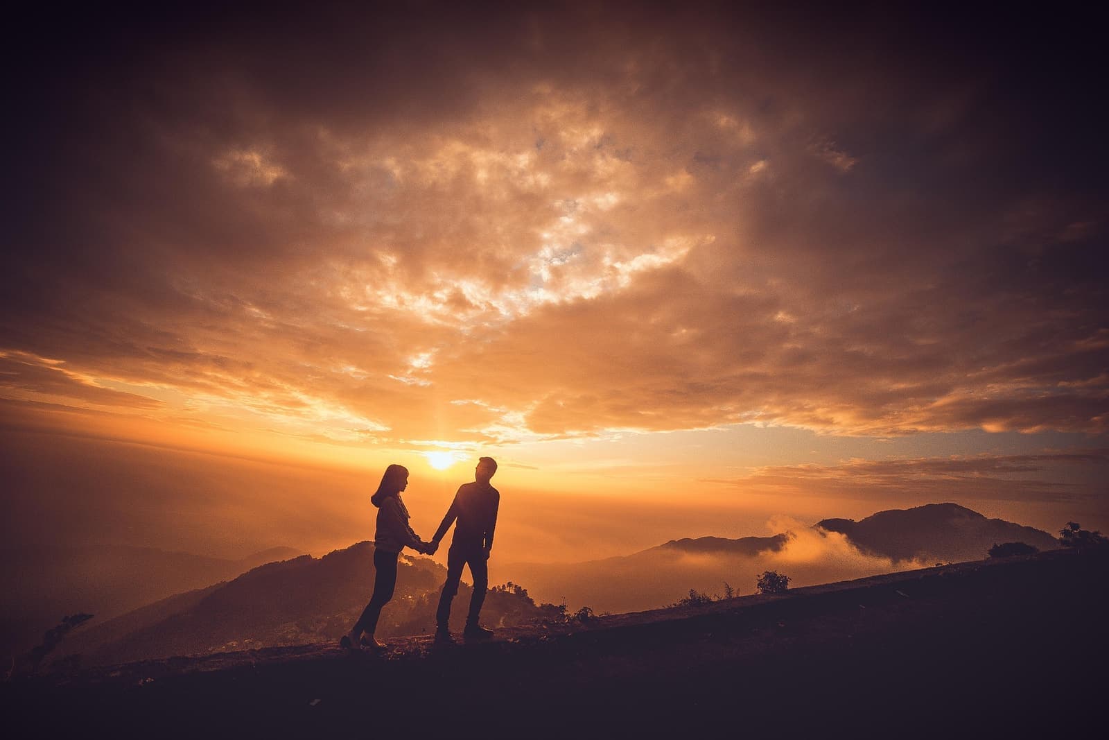 Two silhouettes holding hands on a hilltop under a sunset sky — timing cycles that align, and timing cycles that slip apart