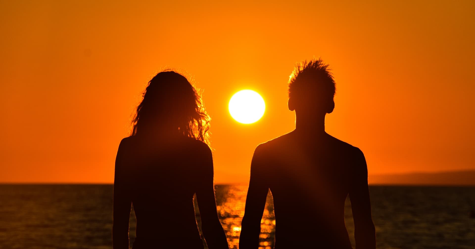 Two silhouettes watching the sun set over the sea — reading yourself, and reading the person you cannot seem to mesh with, from the chart